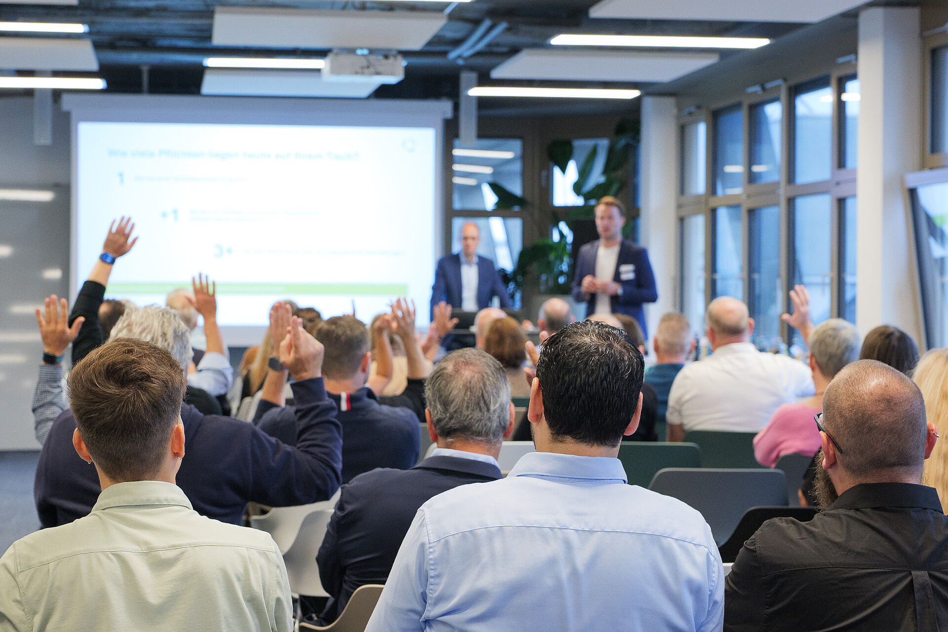 Impression vom audatis MANAGER User-Forum 2026 in Köln Teilnehmer einer Vortragsveranstaltung heben die Hände, um Fragen an die Sprecher zu stellen