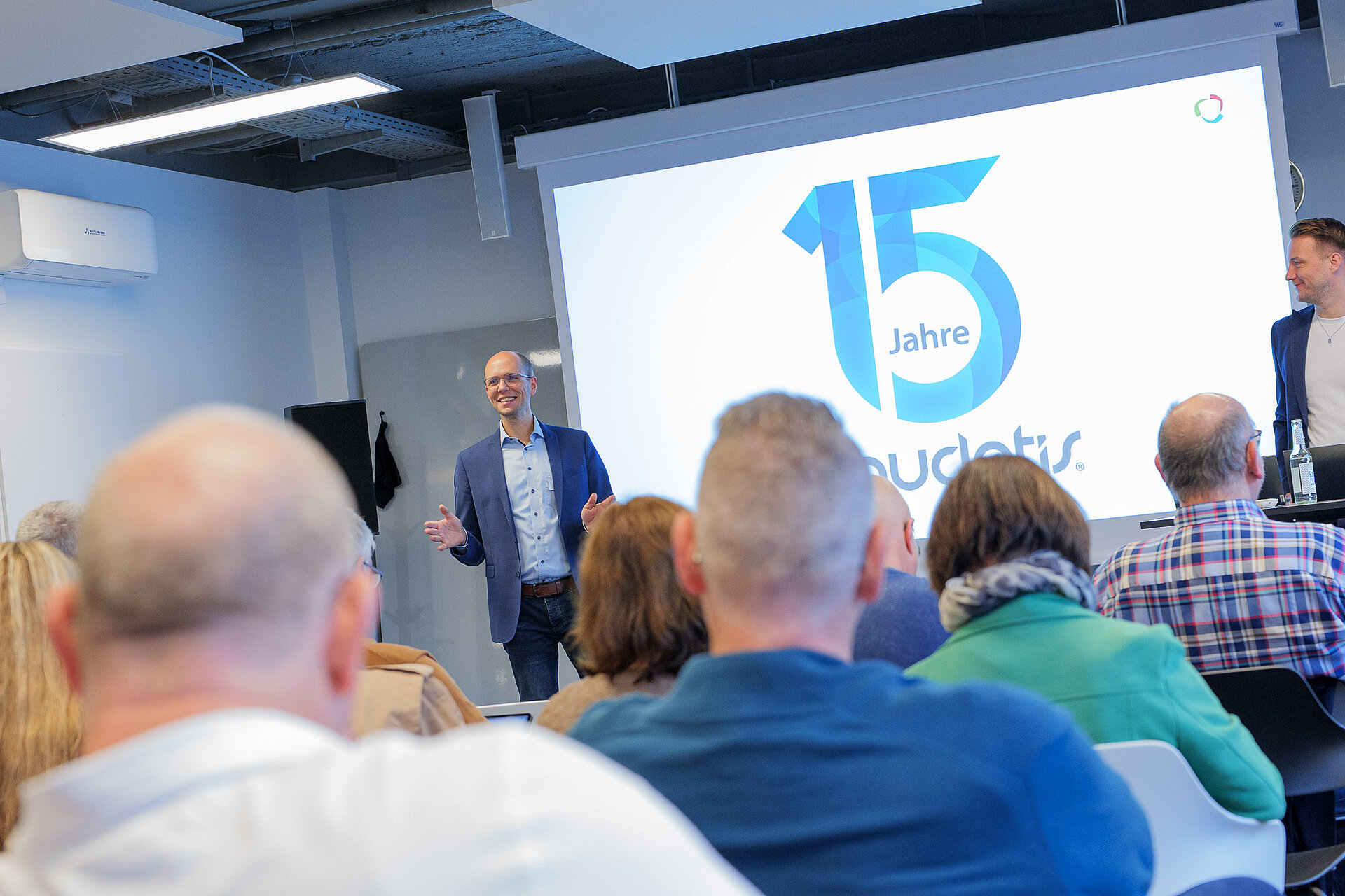 Publikum und Präsentation beim audatis MANAGER User-Forum, auf der Präsentationsfläche steht das Logo zu 15 Jahre audatis